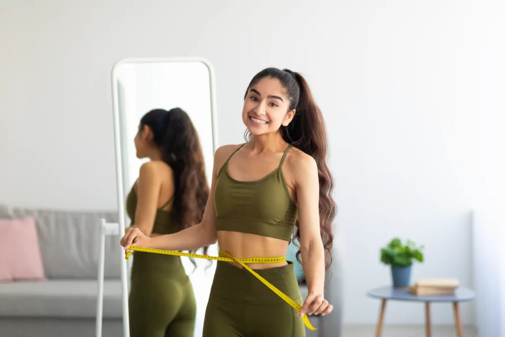 young woman measures waist in home setting utc